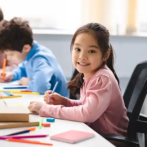 A young girl smiling at camera while working on her assignment